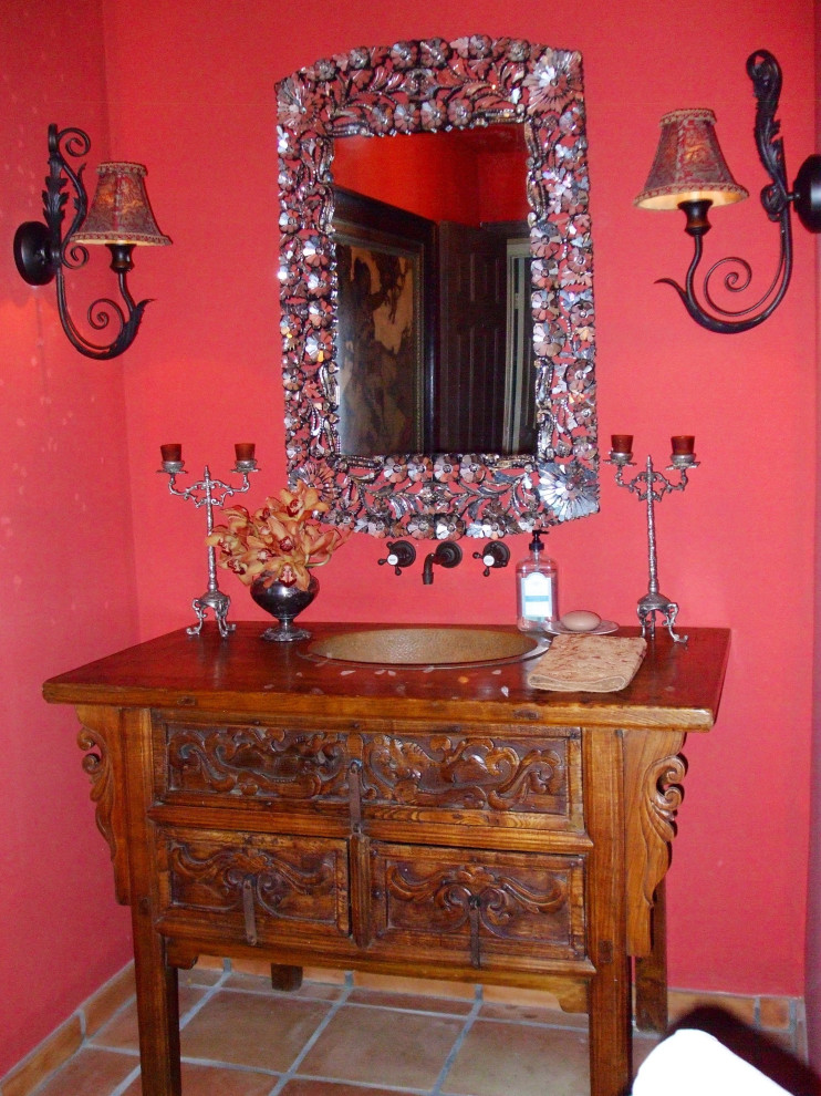 Inspiration for a small country powder room in San Diego with raised-panel cabinets, distressed cabinets, red walls, terra-cotta floors, a drop-in sink, wood benchtops, orange floor, brown benchtops and a freestanding vanity.