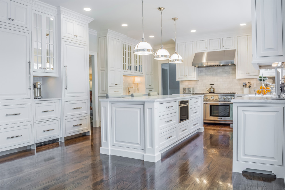This is an example of a large transitional u-shaped kitchen in New York with raised-panel cabinets, white cabinets, marble benchtops, dark hardwood floors and with island.