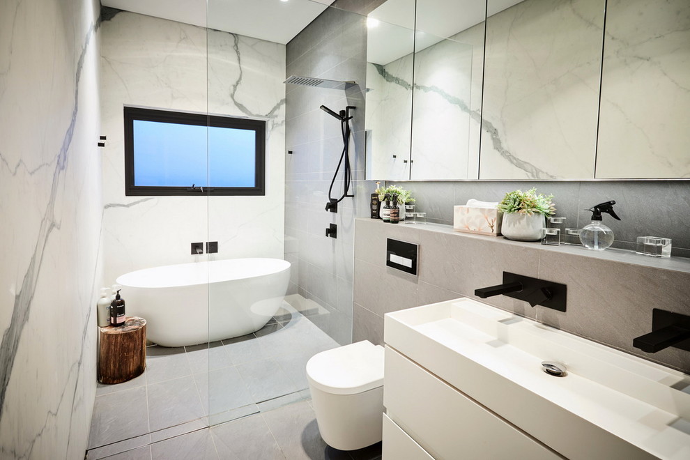Photo of a mid-sized contemporary master bathroom in Sydney with recessed-panel cabinets, white cabinets, a freestanding tub, a shower/bathtub combo, a one-piece toilet, white tile, marble, grey walls, ceramic floors, an integrated sink, engineered quartz benchtops, grey floor, an open shower, white benchtops, a single vanity and a floating vanity.