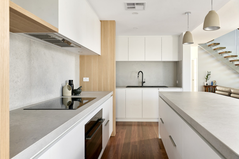 This is an example of a large scandinavian l-shaped eat-in kitchen in Perth with a double-bowl sink, flat-panel cabinets, white cabinets, quartz benchtops, grey splashback, engineered quartz splashback, black appliances, medium hardwood floors, with island, brown floor and grey benchtop.