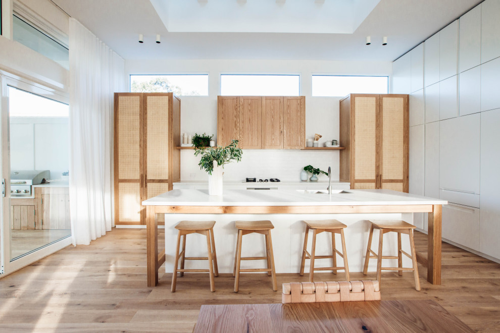 Beach style galley eat-in kitchen in Central Coast with an undermount sink, shaker cabinets, light wood cabinets, white splashback, medium hardwood floors, with island, brown floor and white benchtop.