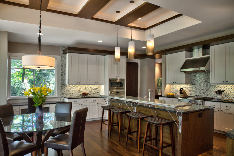 Photo of a mid-sized contemporary u-shaped eat-in kitchen in Minneapolis with shaker cabinets, white cabinets, granite benchtops, multi-coloured splashback, stainless steel appliances, medium hardwood floors, with island, brown floor, black benchtop and vaulted.