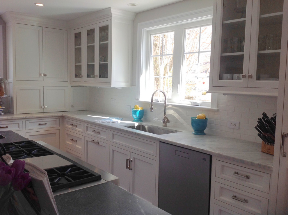 Photo of a large transitional l-shaped open plan kitchen in New York with an undermount sink, recessed-panel cabinets, white cabinets, marble benchtops, white splashback, ceramic splashback, stainless steel appliances, medium hardwood floors and multiple islands.