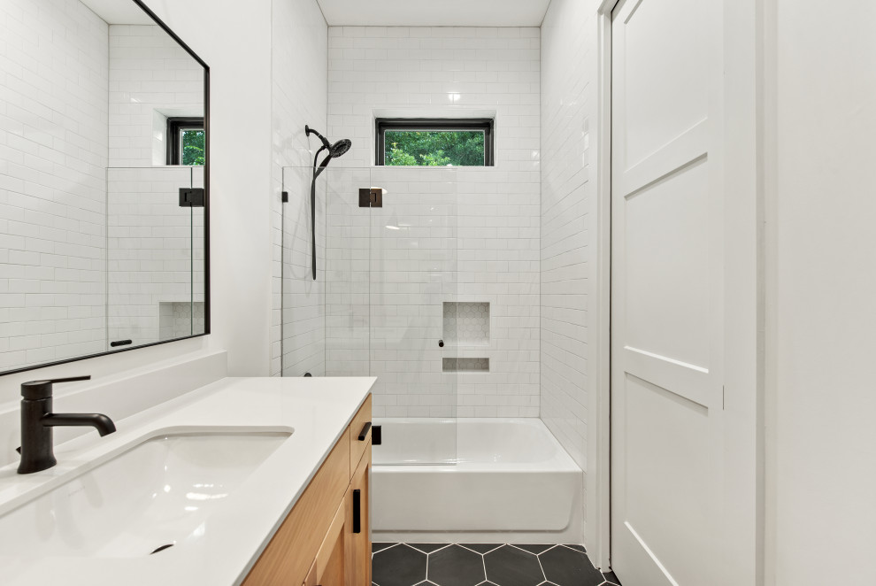 This is an example of a mid-sized scandinavian kids bathroom in Dallas with shaker cabinets, light wood cabinets, an alcove tub, a shower/bathtub combo, a one-piece toilet, white tile, porcelain tile, white walls, cement tiles, an undermount sink, engineered quartz benchtops, black floor, a sliding shower screen, white benchtops, a niche, a double vanity and a built-in vanity.