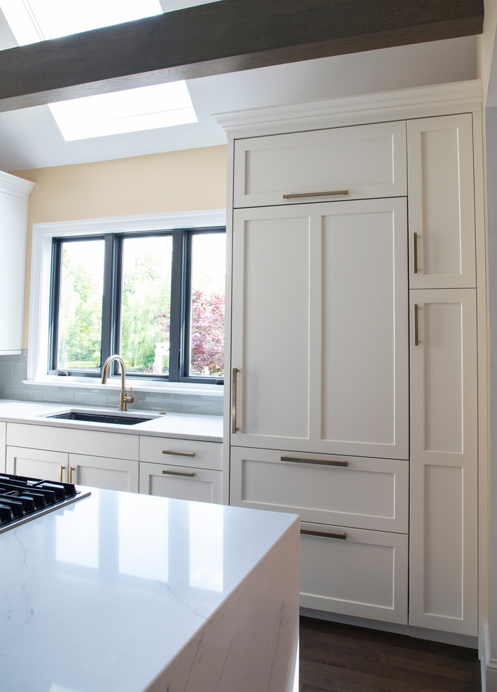 Example of a large transitional u-shaped medium tone wood floor kitchen design with an undermount sink, white cabinets, quartz countertops, gray backsplash, glass tile backsplash, stainless steel appliances, an island and white countertops