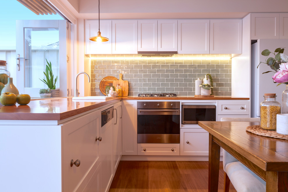 Inspiration for a traditional l-shaped eat-in kitchen in Sydney with a single-bowl sink, shaker cabinets, white cabinets, wood benchtops, grey splashback, subway tile splashback, stainless steel appliances, medium hardwood floors, no island, brown floor and brown benchtop.