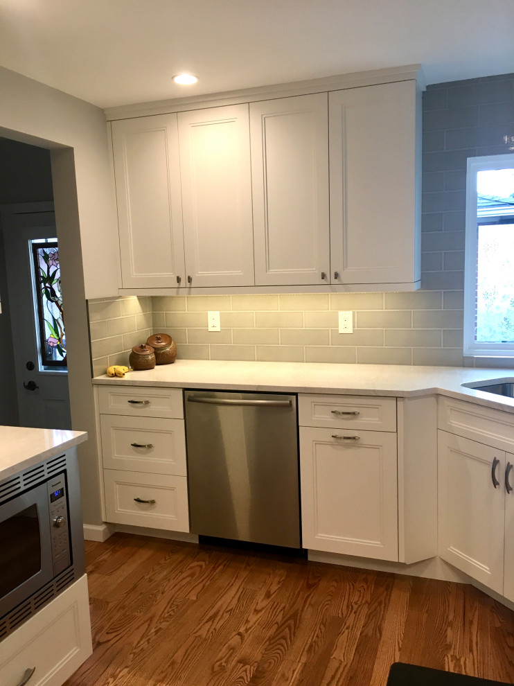 Small transitional u-shaped medium tone wood floor and brown floor enclosed kitchen photo in Denver with a drop-in sink, shaker cabinets, white cabinets, quartz countertops, gray backsplash, subway tile backsplash, stainless steel appliances, a peninsula and white countertops
