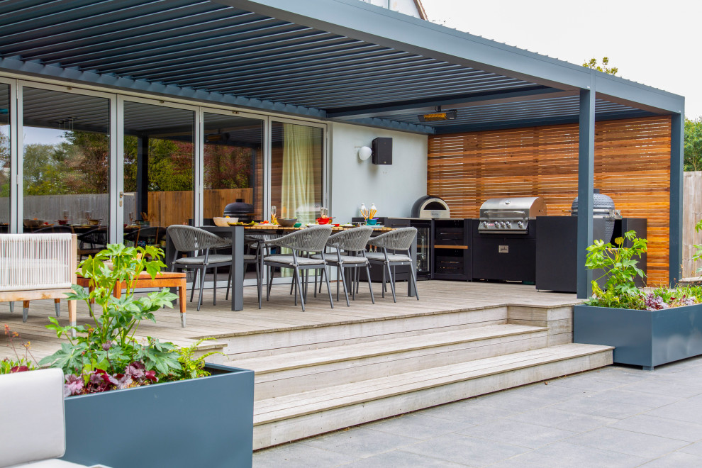 This is an example of a mid-sized contemporary backyard deck in Essex with a pergola.