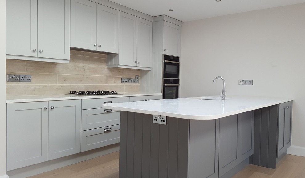 This is an example of a contemporary u-shaped open plan kitchen in Dublin with recessed-panel cabinets, grey cabinets, marble benchtops, beige splashback, porcelain splashback, light hardwood floors and a peninsula.