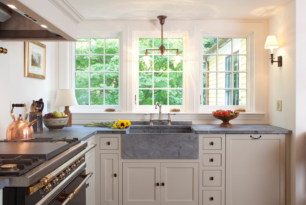 Inspiration for a mid-sized country l-shaped eat-in kitchen in Boston with soapstone benchtops, black appliances, recessed-panel cabinets, a farmhouse sink, green cabinets, beige splashback, ceramic splashback, medium hardwood floors, no island and brown floor.