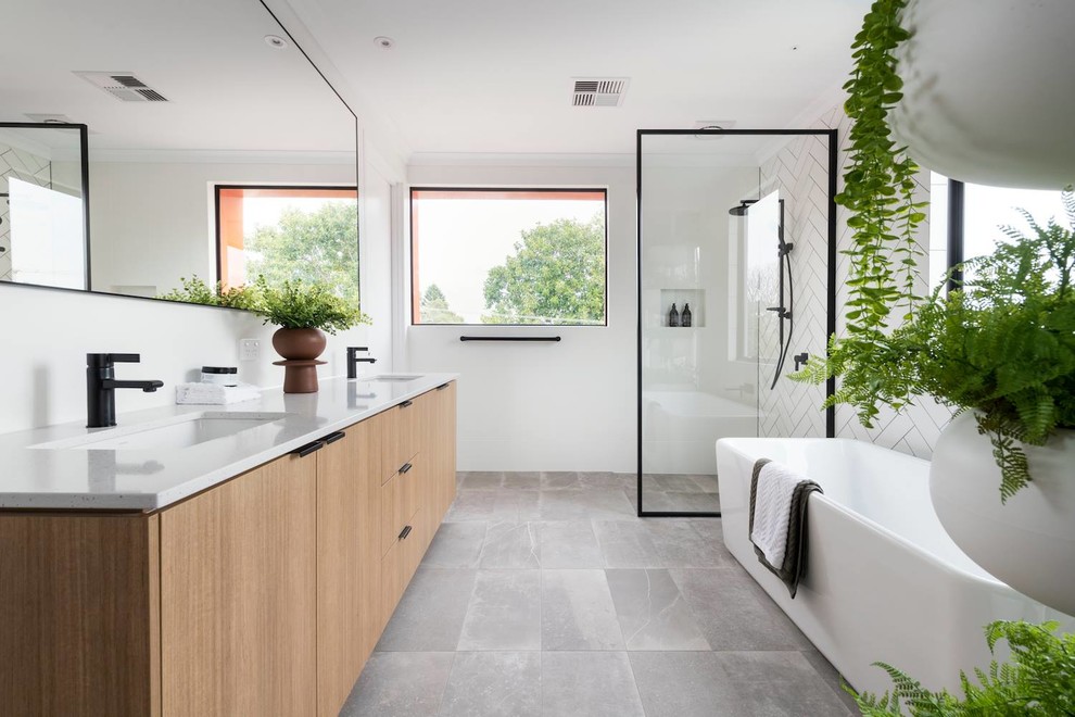 This is an example of a large contemporary master bathroom in Perth with a freestanding tub, white tile, ceramic tile, white walls, cement tiles, engineered quartz benchtops, grey floor, an open shower, medium wood cabinets, a curbless shower, an undermount sink, white benchtops and flat-panel cabinets.