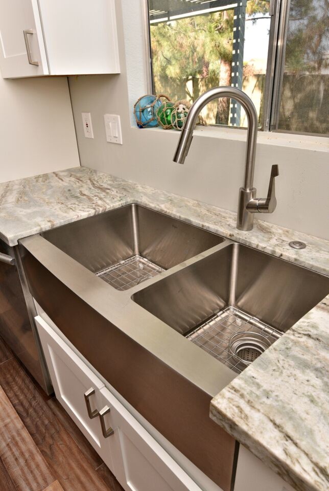 This is an example of a mid-sized beach style l-shaped open plan kitchen in Phoenix with a double-bowl sink, shaker cabinets, white cabinets, stainless steel appliances, medium hardwood floors and with island.