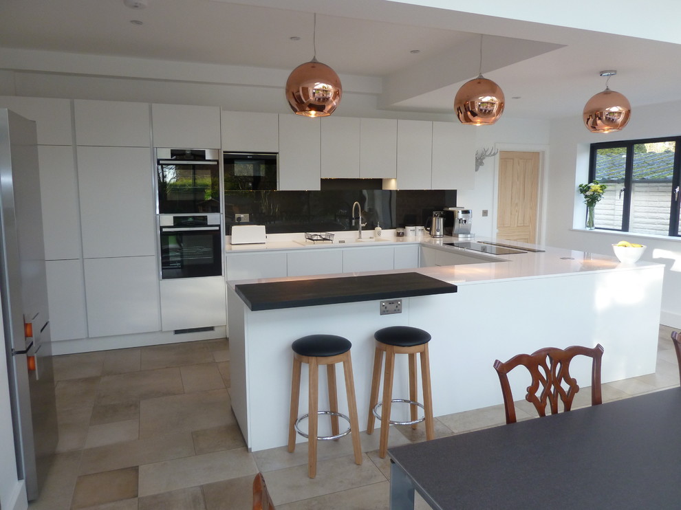 This is an example of a mid-sized contemporary u-shaped eat-in kitchen in Berkshire with flat-panel cabinets, white cabinets, quartzite benchtops, grey splashback and a peninsula.
