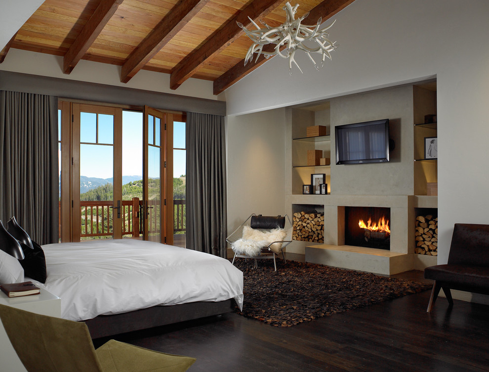 Mid-sized country guest bedroom in Other with white walls, dark hardwood floors, a standard fireplace, a plaster fireplace surround and brown floor.