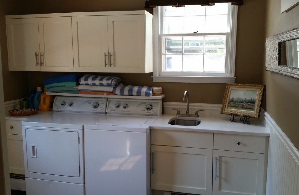 Photo of a mid-sized single-wall laundry room in Philadelphia with an utility sink, white cabinets, marble benchtops, brown walls, vinyl floors and a side-by-side washer and dryer.