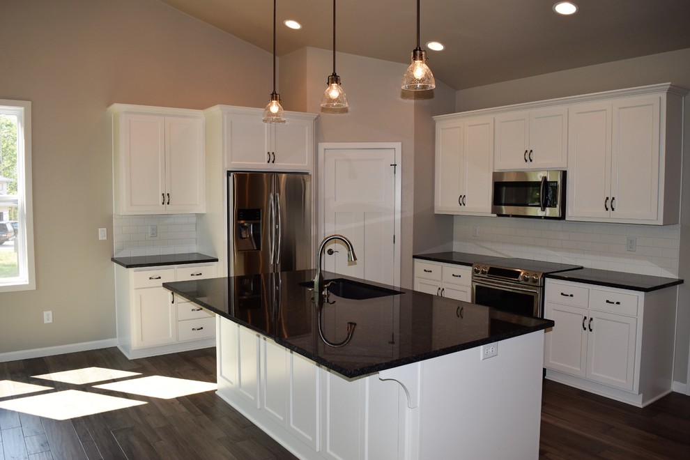 Example of a medium tone wood floor open concept kitchen design with a double-bowl sink, white cabinets, granite countertops, white backsplash, stainless steel appliances and an island