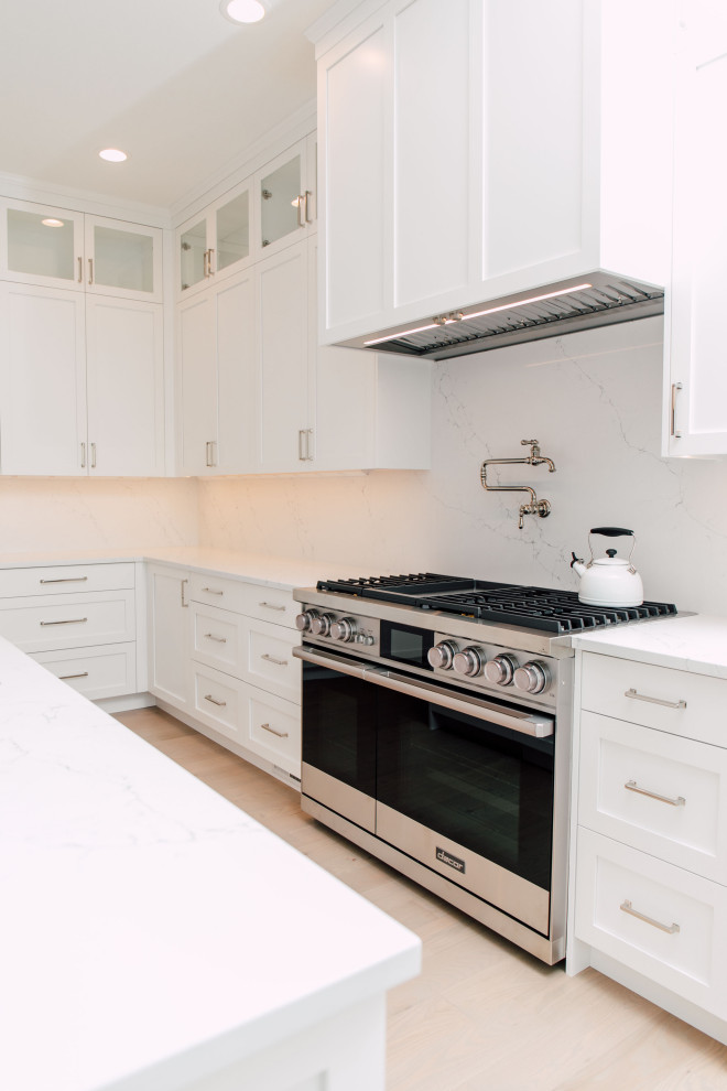 Photo of an expansive contemporary l-shaped eat-in kitchen in Seattle with a single-bowl sink, shaker cabinets, white cabinets, quartz benchtops, white splashback, engineered quartz splashback, panelled appliances, light hardwood floors, multiple islands, beige floor and white benchtop.