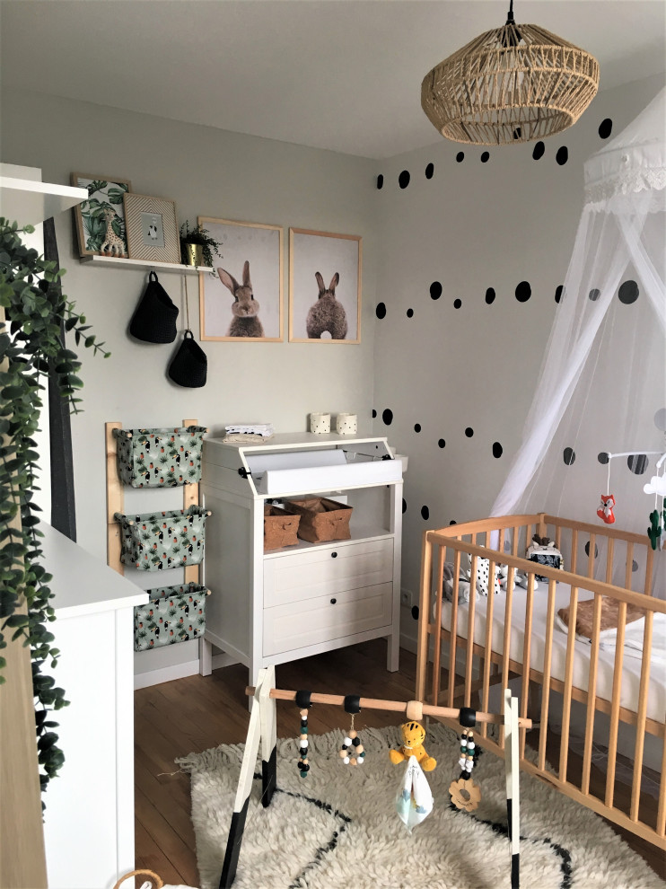 Cette photo montre une chambre de bébé garçon de taille moyenne avec un sol en bois brun et du papier peint.