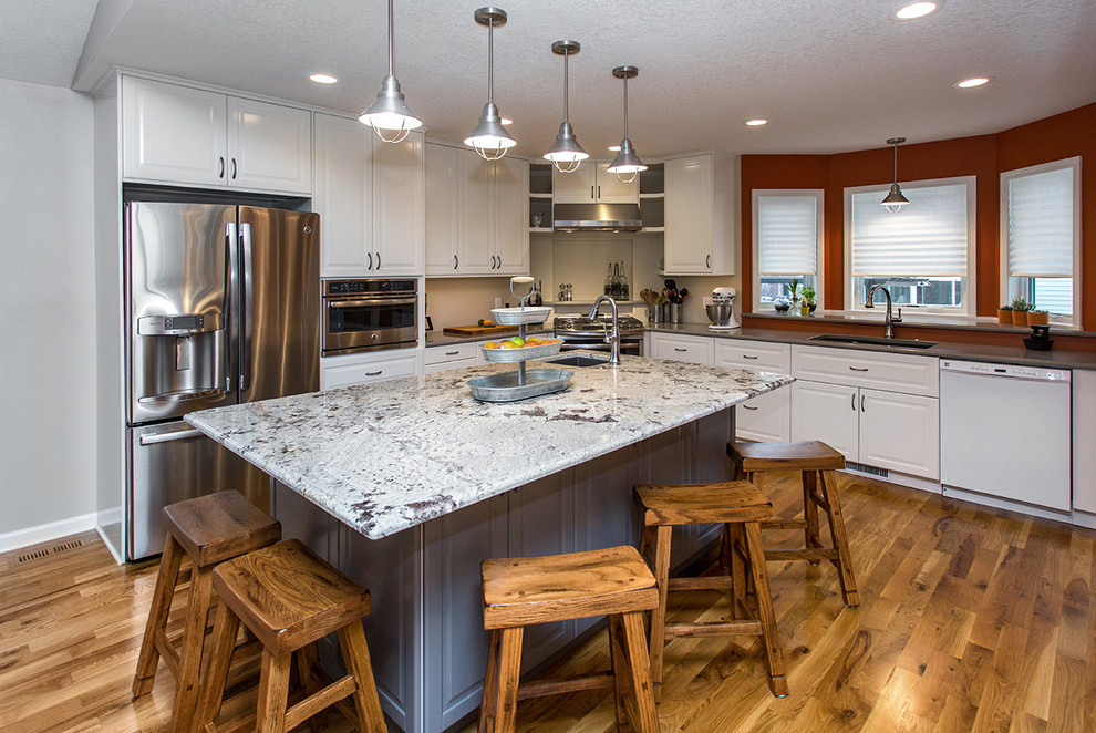 Open concept kitchen - mid-sized transitional u-shaped medium tone wood floor open concept kitchen idea with an undermount sink, raised-panel cabinets, white cabinets, quartz countertops, gray backsplash, stainless steel appliances and an island