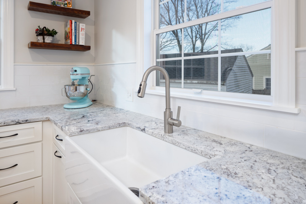 Inspiration for a mid-sized transitional u-shaped medium tone wood floor eat-in kitchen remodel in Boston with a farmhouse sink, shaker cabinets, white cabinets, granite countertops, white backsplash, subway tile backsplash, stainless steel appliances, a peninsula and multicolored countertops