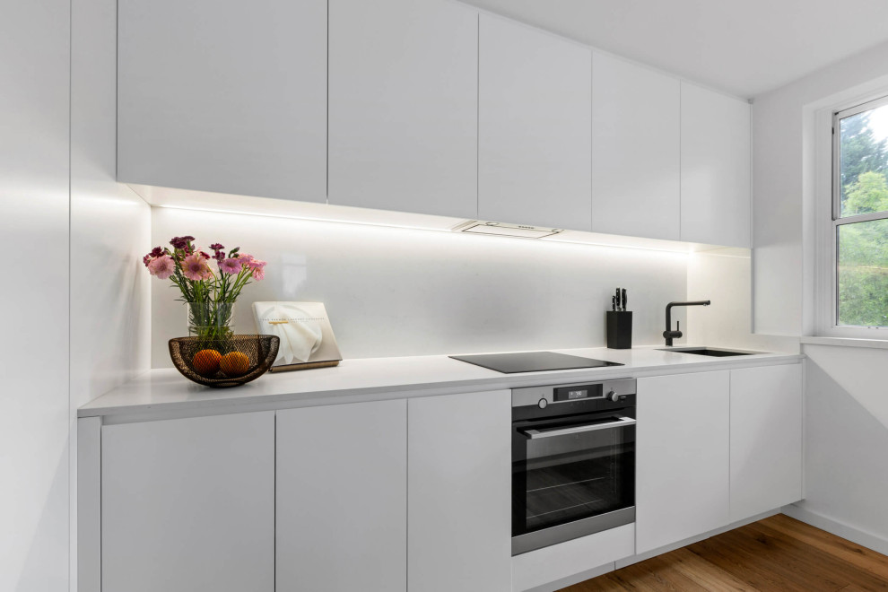 Photo of a small contemporary galley kitchen pantry in Sydney with a drop-in sink, white cabinets, quartz benchtops, white splashback, ceramic splashback, stainless steel appliances, dark hardwood floors, with island, brown floor and white benchtop.