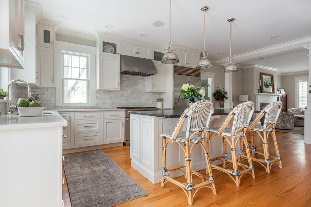 Inspiration for a large transitional u-shaped eat-in kitchen in Boston with an undermount sink, shaker cabinets, white cabinets, quartz benchtops, grey splashback, subway tile splashback, stainless steel appliances, medium hardwood floors, with island, brown floor and black benchtop.