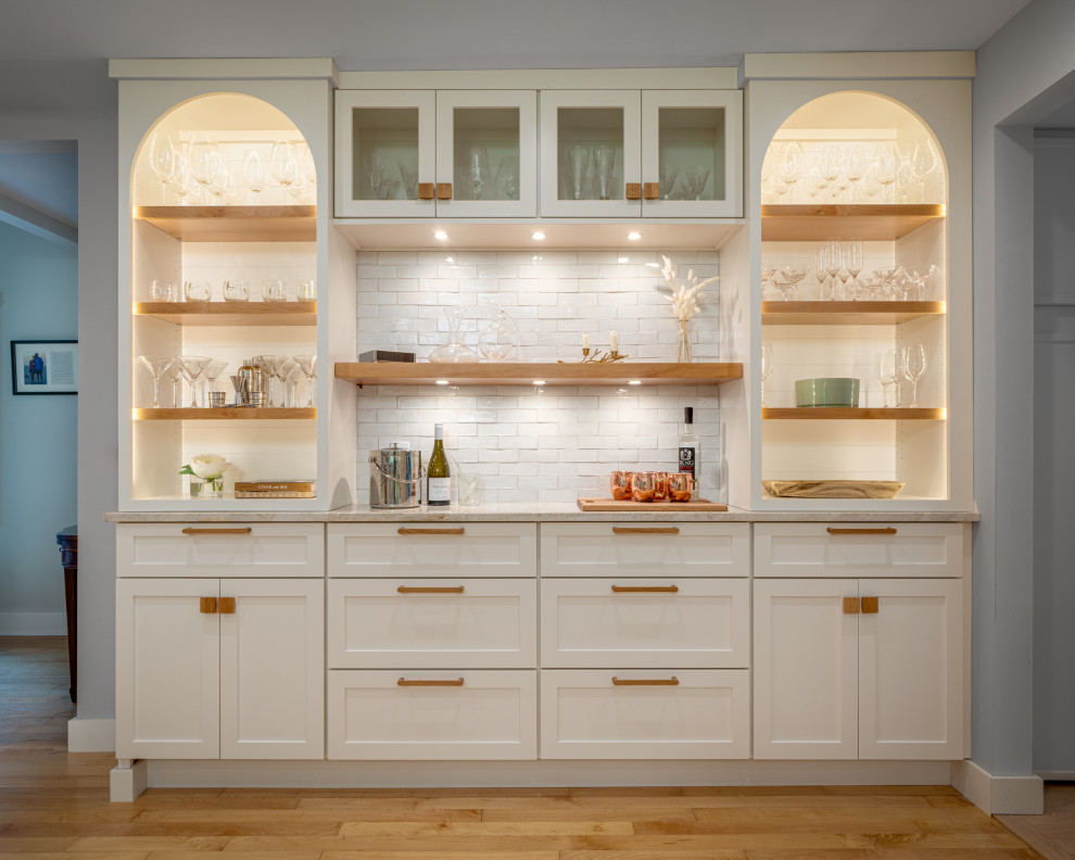 Photo of a mid-sized eclectic single-wall home bar in Other with shaker cabinets, white cabinets, quartzite benchtops, white splashback, terra-cotta splashback, light hardwood floors and beige benchtop.