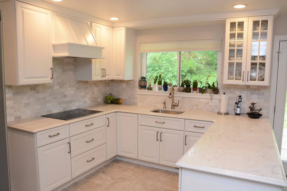 Photo of a mid-sized transitional u-shaped separate kitchen in DC Metro with an undermount sink, raised-panel cabinets, white cabinets, quartz benchtops, white splashback, stainless steel appliances, a peninsula, beige floor and white benchtop.