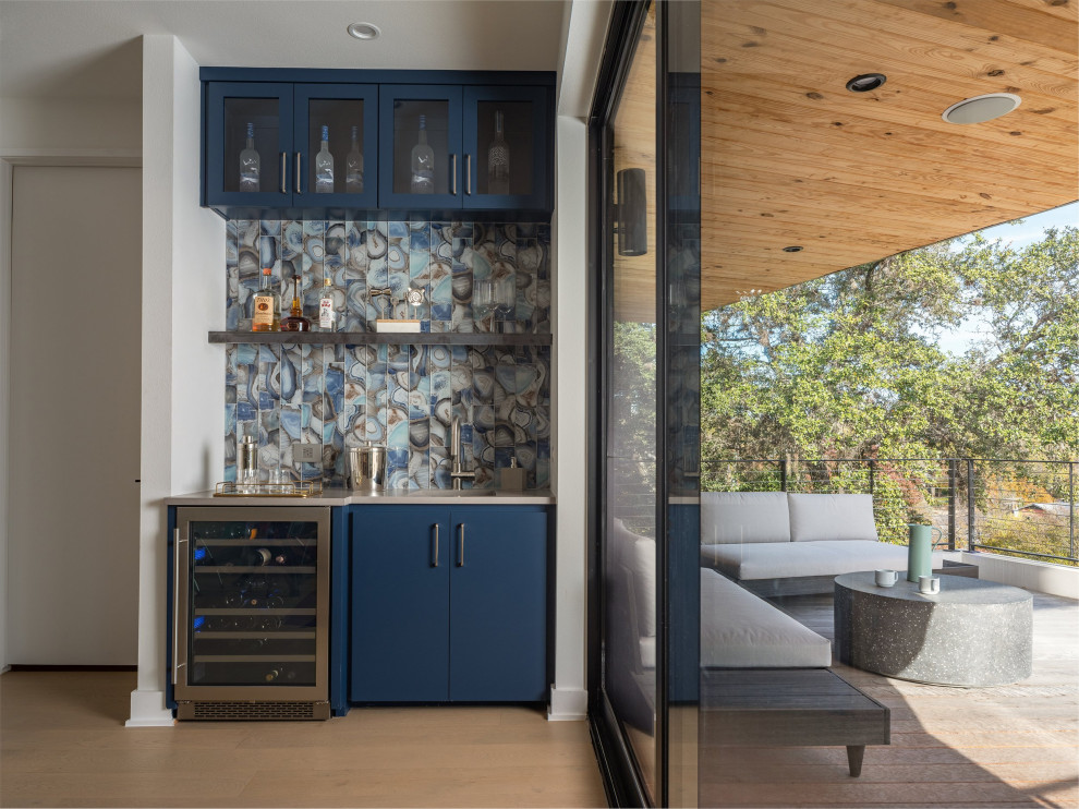 Inspiration for a small contemporary single-wall wet bar in Austin with an undermount sink, glass-front cabinets, blue cabinets, quartz benchtops, blue splashback, glass tile splashback, light hardwood floors and grey benchtop.