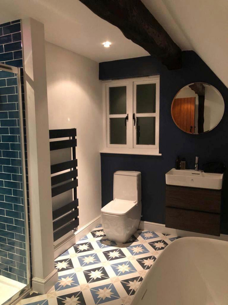 Photo of a mid-sized contemporary kids bathroom in Hertfordshire with flat-panel cabinets, dark wood cabinets, a freestanding tub, a curbless shower, a one-piece toilet, blue tile, ceramic tile, blue walls, porcelain floors, a wall-mount sink, solid surface benchtops, a sliding shower screen, a niche, a single vanity, a floating vanity and vaulted.