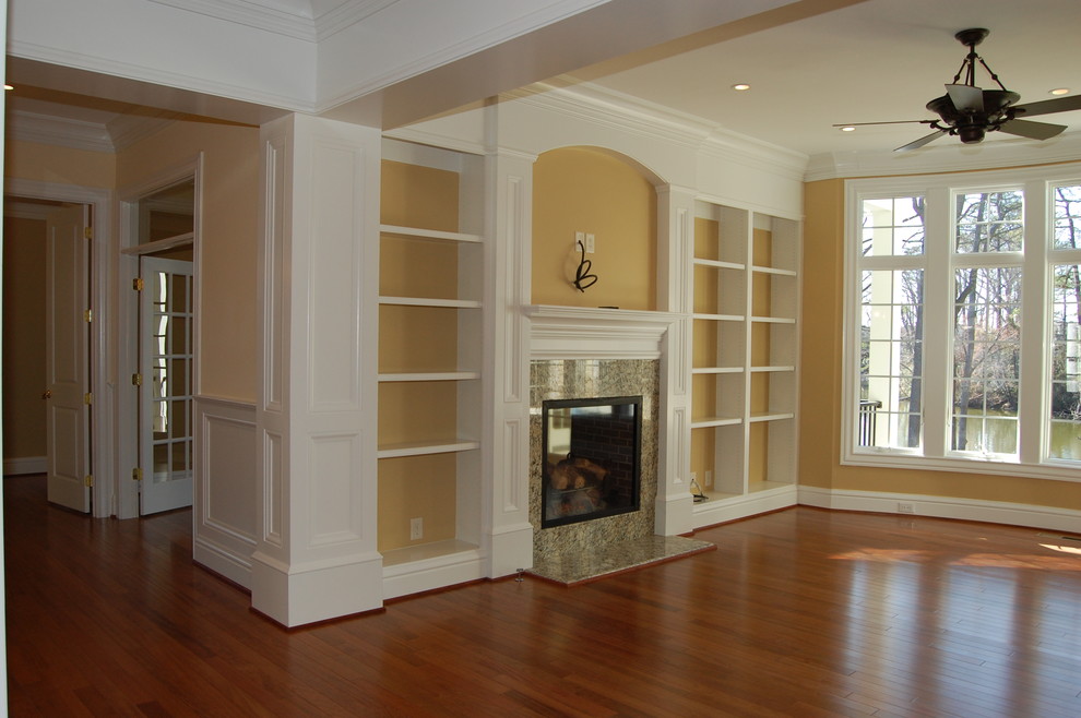 Inspiration for a traditional enclosed family room in Other with a library, yellow walls, medium hardwood floors, a standard fireplace, a stone fireplace surround and a wall-mounted tv.