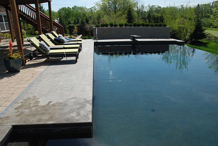 Large modern backyard rectangular infinity pool in Chicago with concrete slab.