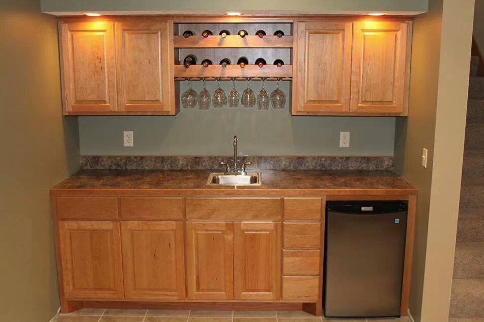 Photo of a small traditional single-wall wet bar in Minneapolis with an undermount sink, raised-panel cabinets, light wood cabinets, laminate benchtops, green splashback, laminate floors, brown floor and multi-coloured benchtop.