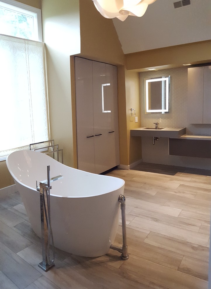 Photo of a large modern master bathroom in Philadelphia with beige walls, light hardwood floors, an integrated sink, beige floor, a freestanding tub, an alcove shower, flat-panel cabinets, white cabinets, gray tile, white tile, marble, concrete benchtops and a hinged shower door.