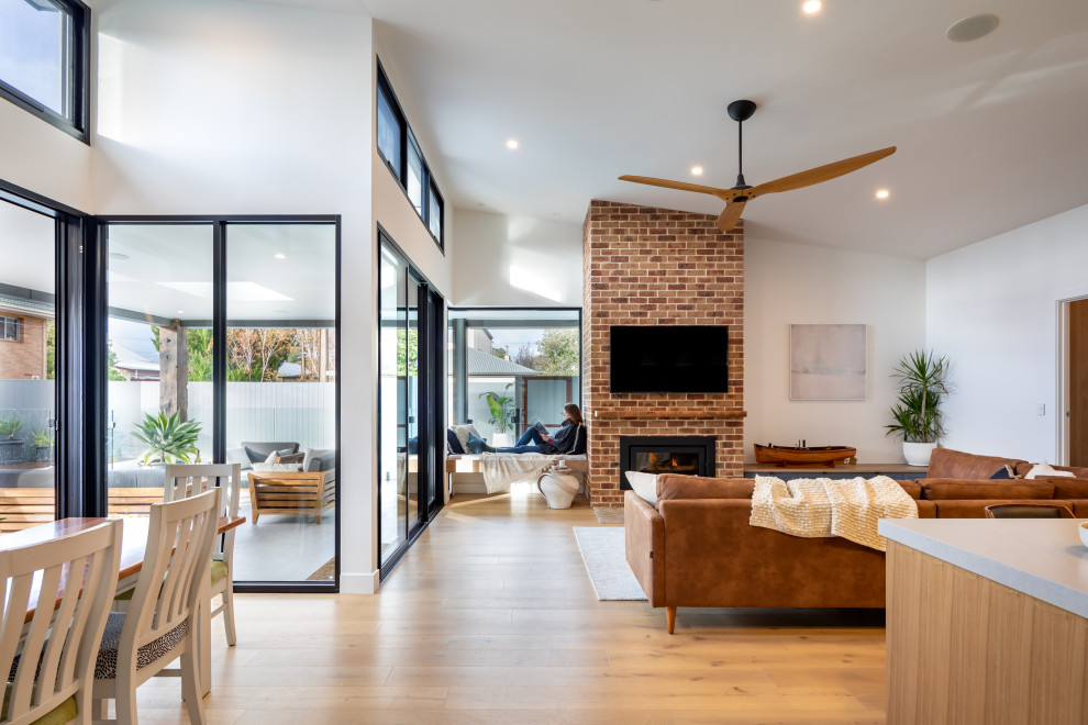 Large contemporary open concept living room in Adelaide with white walls, a brick fireplace surround, a wall-mounted tv, brown floor, medium hardwood floors, a standard fireplace and vaulted.