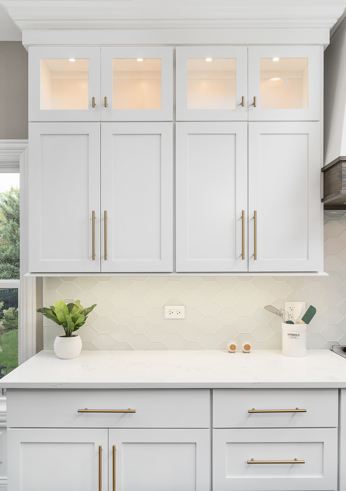 This is an example of a mid-sized transitional single-wall open plan kitchen in Chicago with white cabinets, quartz benchtops, white splashback, stainless steel appliances, dark hardwood floors, with island, brown floor, white benchtop, a farmhouse sink, shaker cabinets and glass tile splashback.