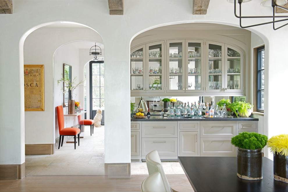 Small transitional single-wall wet bar in New York with an undermount sink, shaker cabinets, white cabinets, mirror splashback and travertine floors.