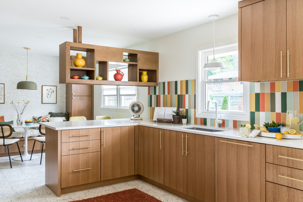 Cette image montre une cuisine encastrable vintage en bois brun avec un évier encastré, un placard à porte plane, une crédence multicolore, une péninsule, un sol beige et un plan de travail blanc.