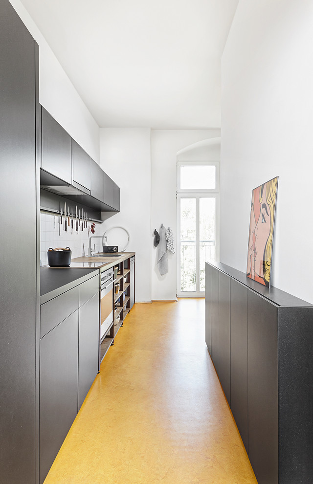 Photo of a small contemporary single-wall separate kitchen in Leipzig with a drop-in sink, flat-panel cabinets, grey cabinets, white splashback, stainless steel appliances, no island and yellow floor.