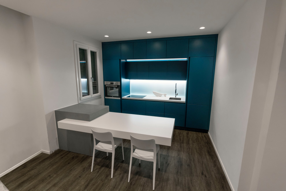 Immagine di una piccola cucina moderna con lavello a vasca singola, ante a filo, ante blu, top in laminato, paraspruzzi con piastrelle di vetro, elettrodomestici in acciaio inossidabile, parquet scuro, pavimento marrone e top bianco