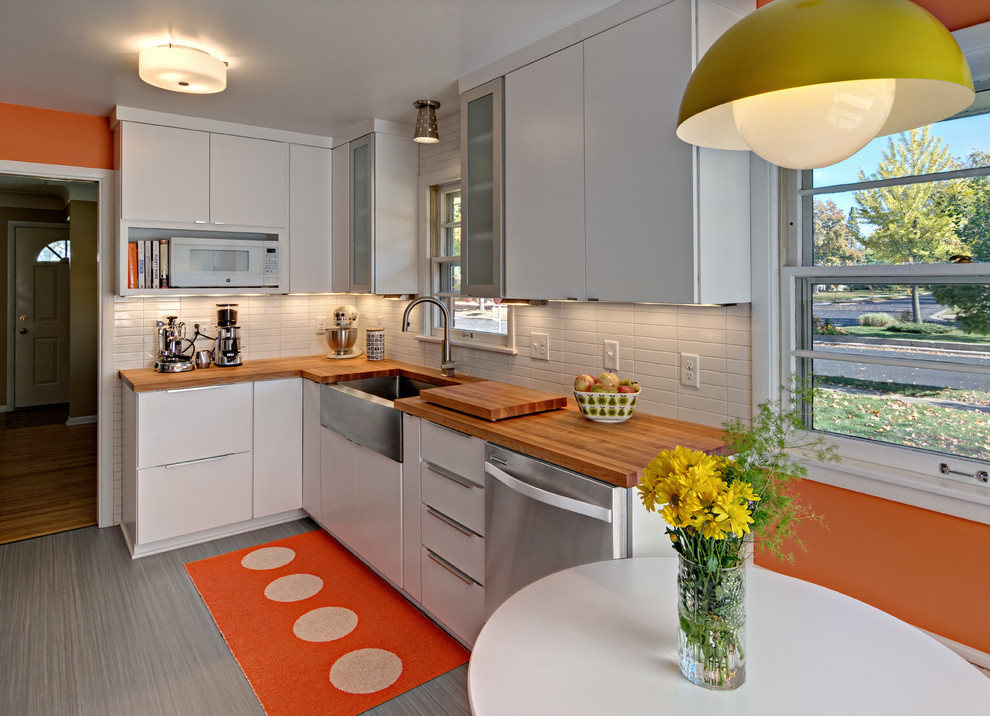 Design ideas for a small midcentury u-shaped eat-in kitchen in Minneapolis with a farmhouse sink, flat-panel cabinets, white cabinets, wood benchtops, white splashback, ceramic splashback, linoleum floors, no island and stainless steel appliances.