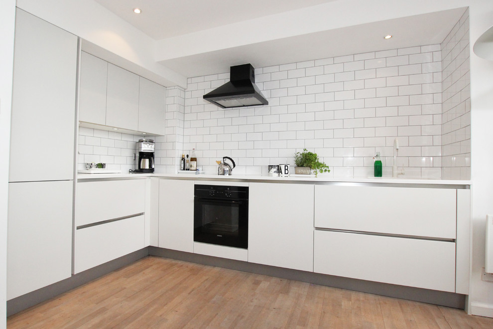 Modern l-shaped kitchen in London with flat-panel cabinets, white cabinets, white splashback and subway tile splashback.
