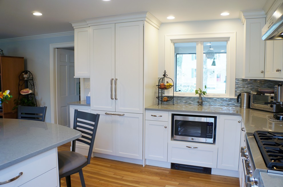 Inspiration for a mid-sized transitional l-shaped light wood floor eat-in kitchen remodel in Boston with a farmhouse sink, shaker cabinets, white cabinets, quartz countertops, blue backsplash, glass tile backsplash, paneled appliances and a peninsula