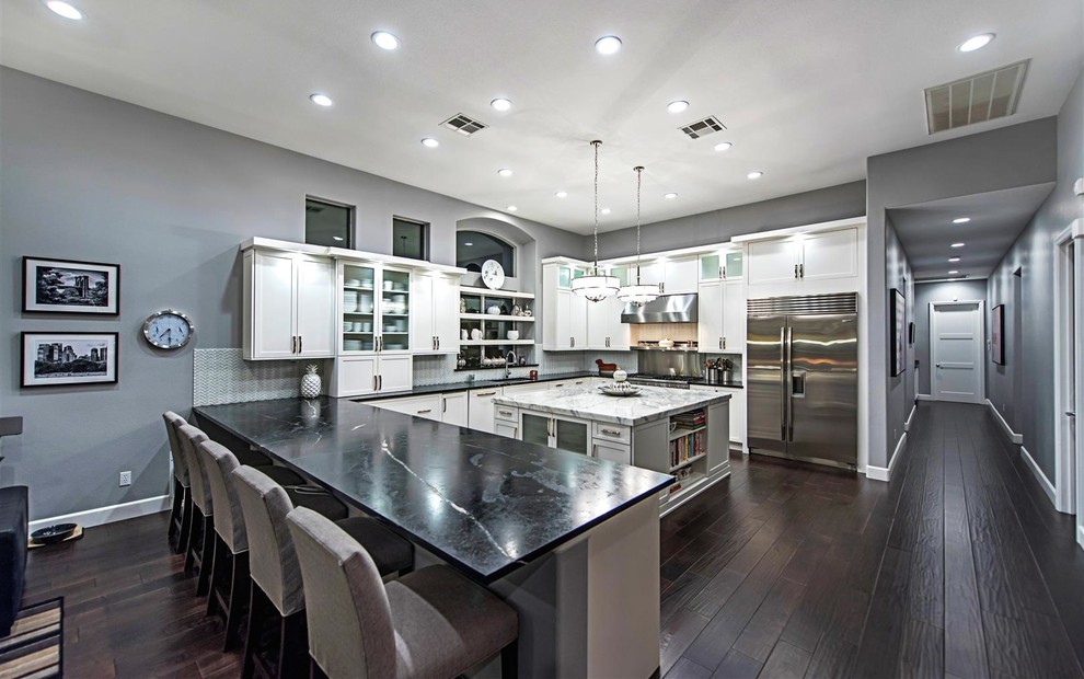 Inspiration for an expansive transitional u-shaped open plan kitchen in Las Vegas with an undermount sink, shaker cabinets, white cabinets, white splashback, ceramic splashback, stainless steel appliances, dark hardwood floors and with island.