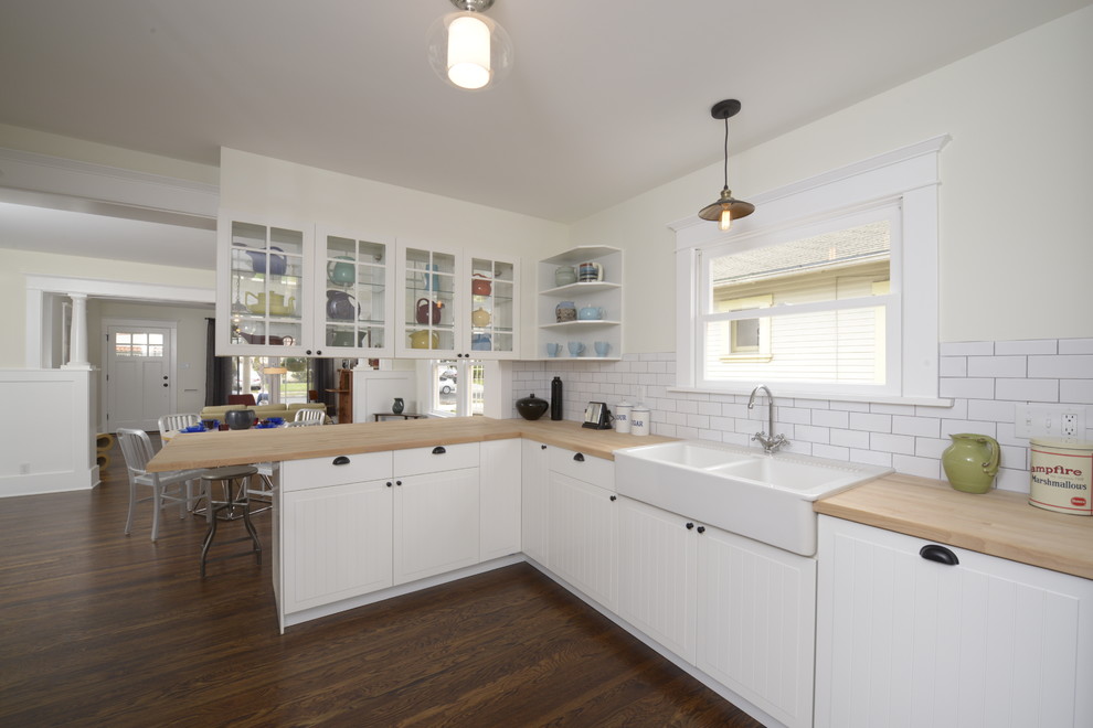 Photo of a mid-sized arts and crafts u-shaped eat-in kitchen in Los Angeles with a peninsula, beaded inset cabinets, white cabinets, wood benchtops, white splashback, subway tile splashback, panelled appliances, a farmhouse sink and dark hardwood floors.