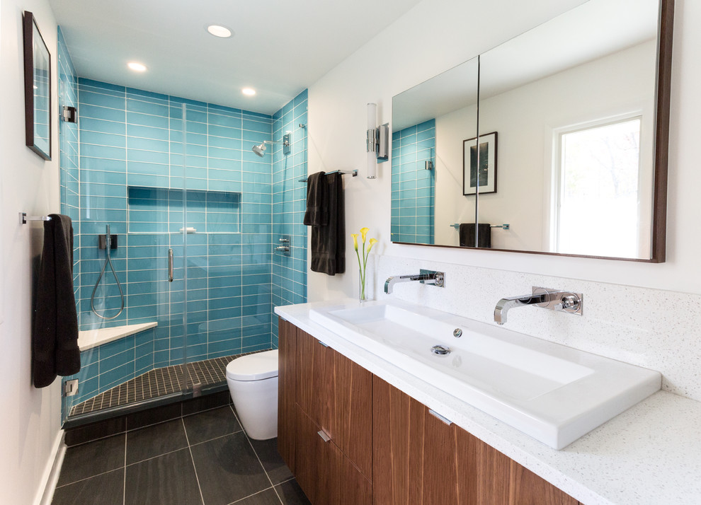 Mid-sized contemporary master bathroom in New York with flat-panel cabinets, an alcove shower, a one-piece toilet, blue tile, glass tile, white walls, porcelain floors, engineered quartz benchtops, dark wood cabinets and a trough sink.