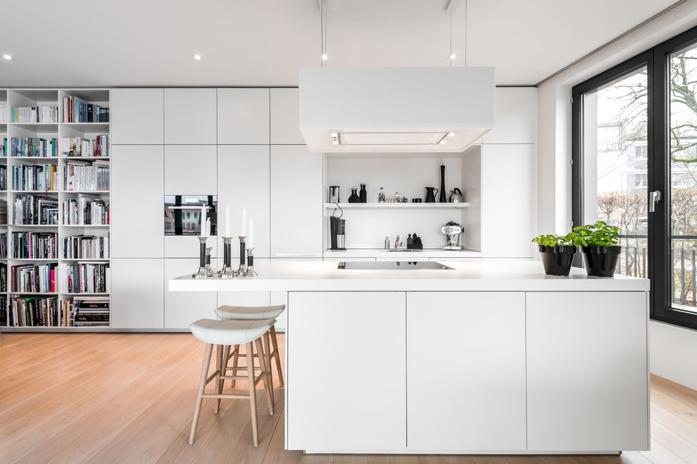 This is an example of a modern single-wall open plan kitchen in Hamburg with flat-panel cabinets, white cabinets, solid surface benchtops, white splashback, light hardwood floors, with island, white benchtop, a single-bowl sink and beige floor.