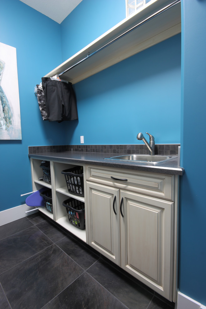 Inspiration for a small contemporary galley dedicated laundry room in Other with a drop-in sink, raised-panel cabinets, white cabinets, laminate benchtops, blue walls, a side-by-side washer and dryer, terra-cotta floors and grey floor.