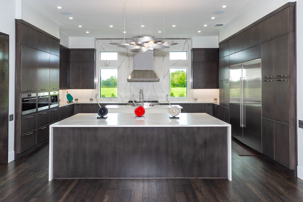 Photo of a contemporary u-shaped open plan kitchen in Tampa with flat-panel cabinets, dark wood cabinets, white splashback, stone slab splashback, stainless steel appliances, dark hardwood floors, multiple islands, brown floor and white benchtop.