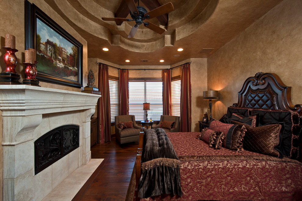 Photo of an expansive mediterranean master bedroom in Austin with beige walls, dark hardwood floors, a standard fireplace and a stone fireplace surround.